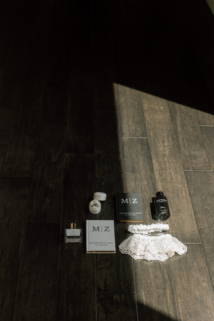 wedding flat lay details photo with vow books, rings, perfume, cologne, and garter