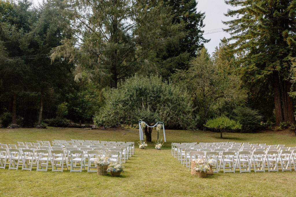 wedding ceremony with trees and white chairs and summer colorful flowers setup by wedding planner