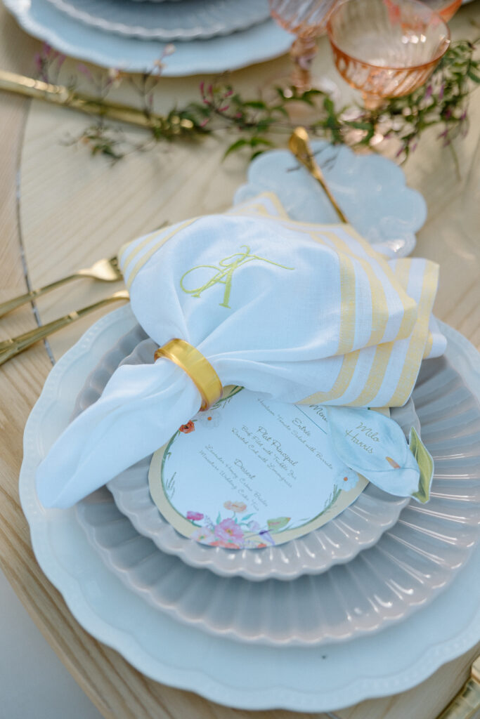 Amalfi Coast–inspired wedding tablescape at Château St. Jean featuring yellow striped linens, fresh citrus, embroidered monogram napkins, and lush floral design