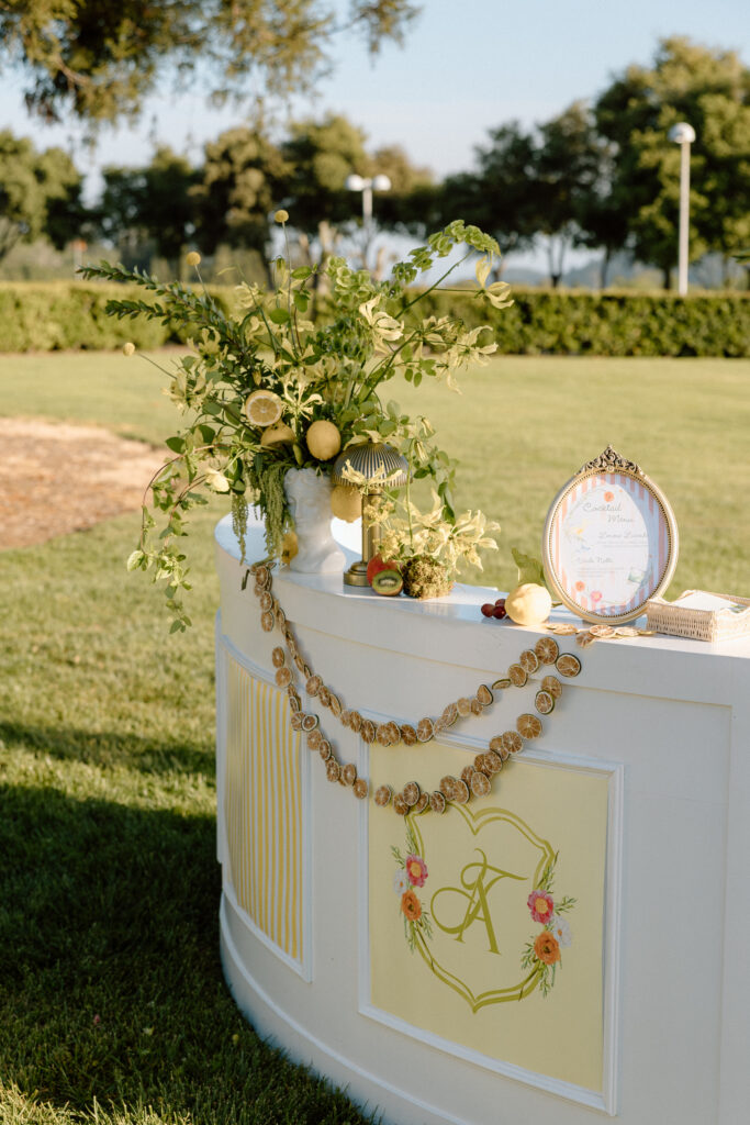 European-inspired wedding cocktail hour at Château St. Jean with citrus details, statement signage, striped linens, and a ‘ring for champagne’ moment in Sonoma Valley.