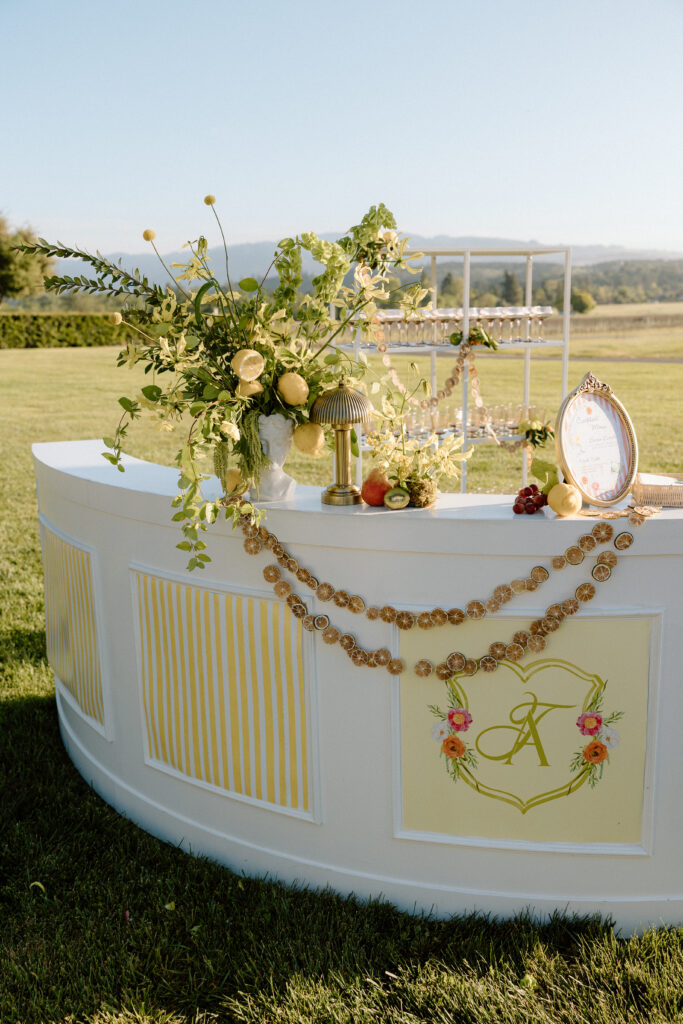 European-inspired wedding cocktail hour at Château St. Jean with citrus details, statement signage, striped linens, and a ‘ring for champagne’ moment in Sonoma Valley.
