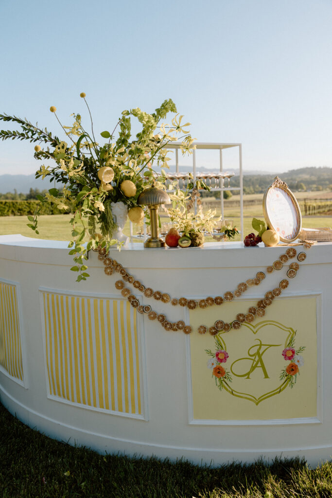 European-inspired wedding cocktail hour at Château St. Jean with citrus details, statement signage, striped linens, and a ‘ring for champagne’ moment in Sonoma Valley.