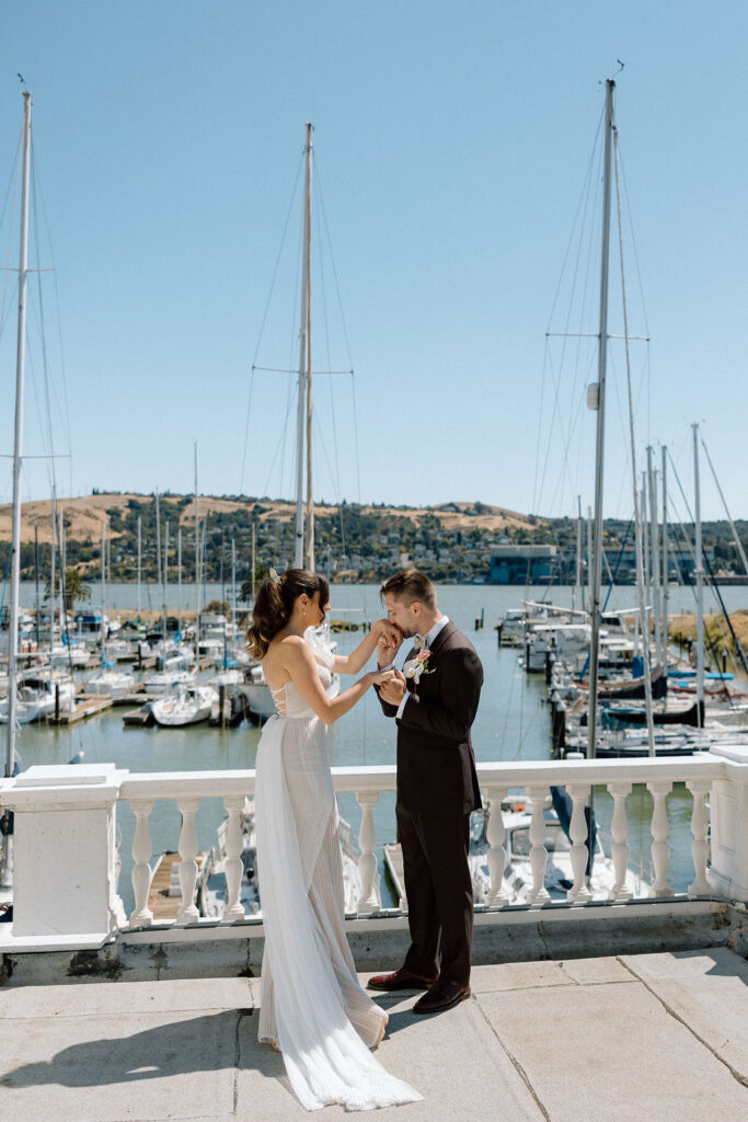 Bride and groom embracing during their first look on a marina balcony surrounded by sailboats