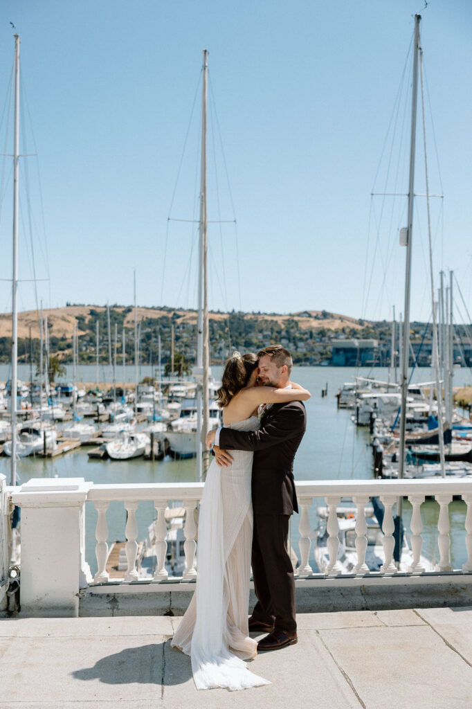 Bride and groom embracing during their first look on a marina balcony surrounded by sailboats
