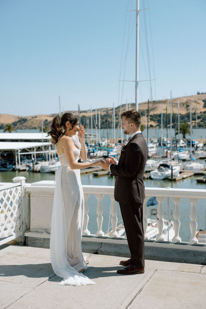 Bride and groom embracing during their first look on a marina balcony surrounded by sailboats