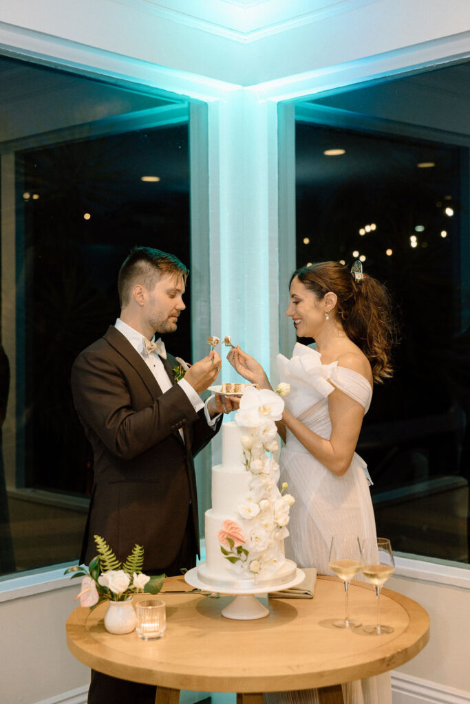 Bride and groom cutting their wedding cake inside the reception space following a sailboat ceremony exit