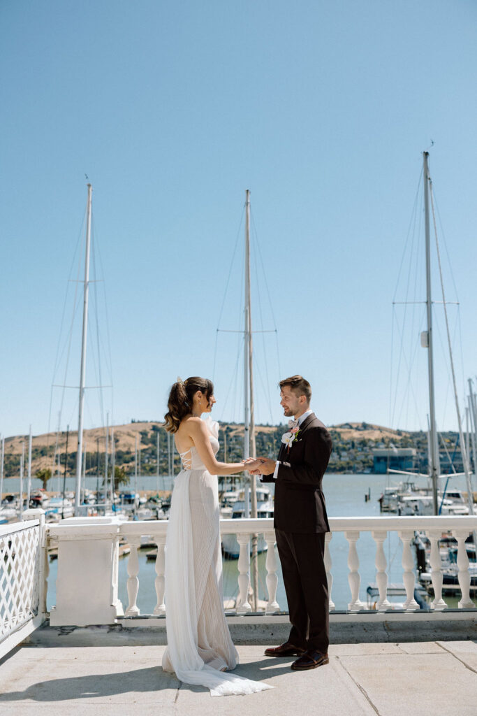 Bride and groom embracing during their first look on a marina balcony surrounded by sailboats