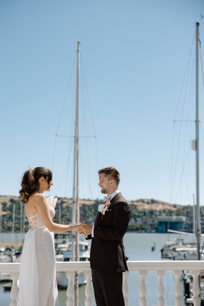 Bride and groom embracing during their first look on a marina balcony surrounded by sailboats