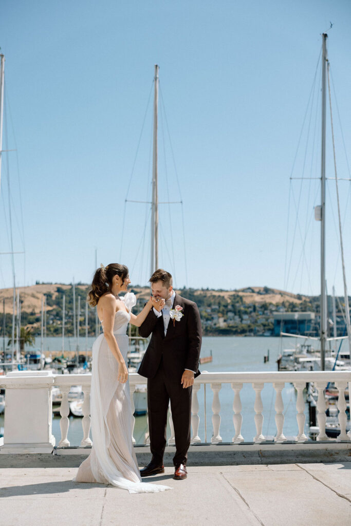 Bride and groom embracing during their first look on a marina balcony surrounded by sailboats