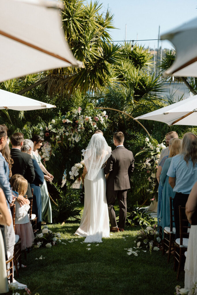 Bride and groom exchanging vows during an outdoor ceremony at Glen Cove Marina, surrounded by palm trees and sailboats in Northern California