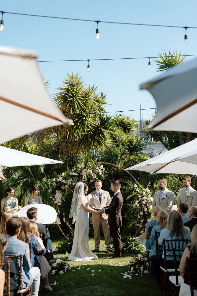 Bride and groom exchanging vows during an outdoor ceremony at Glen Cove Marina, surrounded by palm trees and sailboats in Northern California