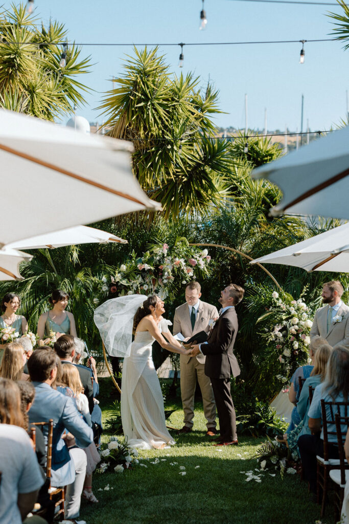 Bride and groom exchanging vows during an outdoor ceremony at Glen Cove Marina, surrounded by palm trees and sailboats in Northern California
