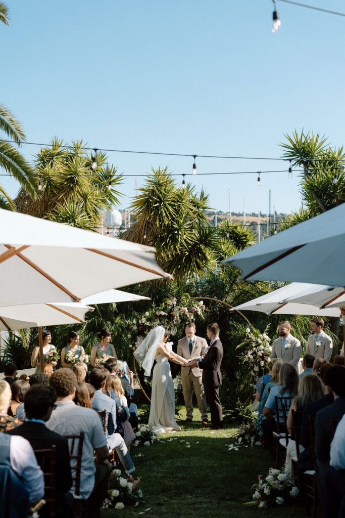 Bride and groom exchanging vows during an outdoor ceremony at Glen Cove Marina, surrounded by palm trees and sailboats in Northern California