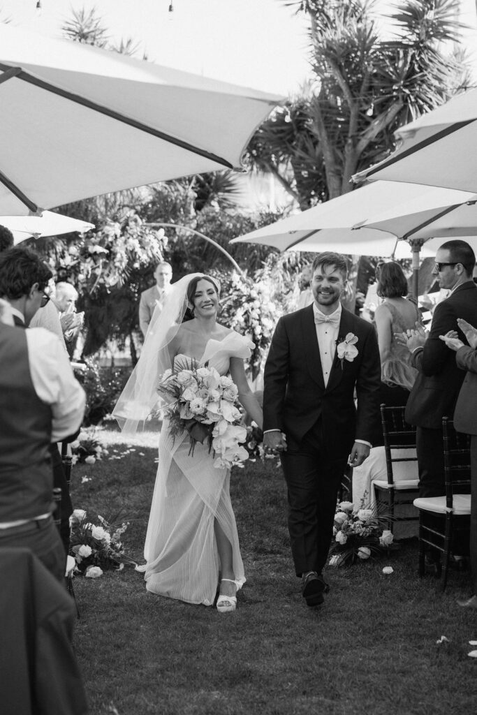 Newly married couple walking hand-in-hand from their ceremony to a sailboat dock at a Northern California marina wedding