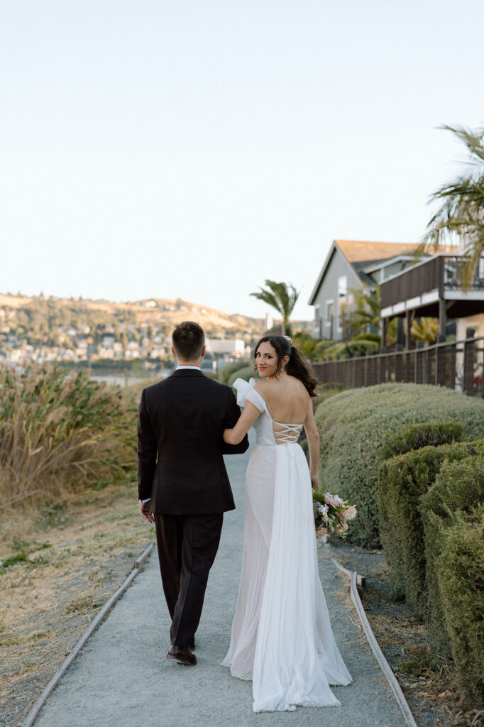 Bride and groom walking hand-in-hand near the water at sunset during their Glen Cove Marina wedding