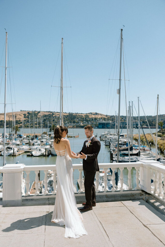Bride and groom embracing during their first look on a marina balcony surrounded by sailboats