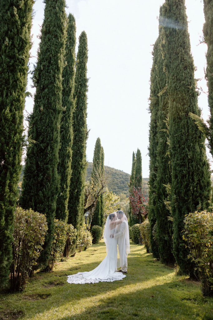 Bride and groom walking through the gardens of Villa di Piazzano in Tuscany, surrounded by cypress trees and rolling hills during an intimate destination wedding.