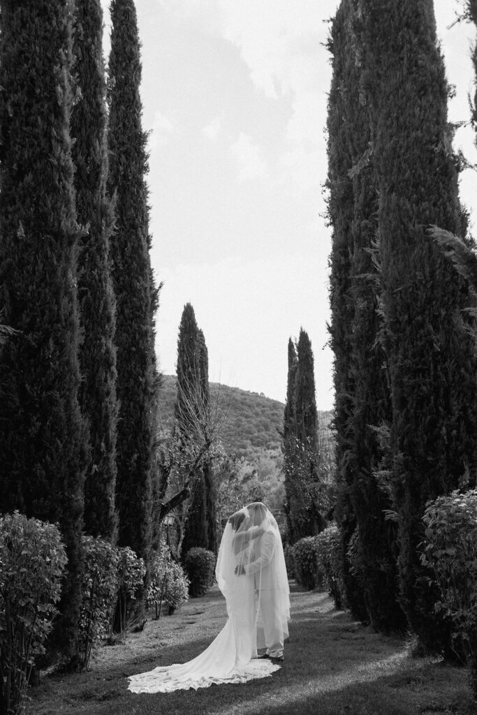 Bride and groom walking through the gardens of Villa di Piazzano in Tuscany, surrounded by cypress trees and rolling hills during an intimate destination wedding.