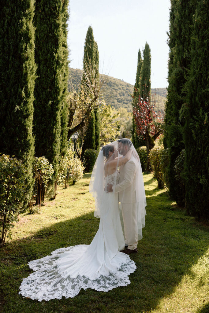 Bride and groom walking through the gardens of Villa di Piazzano in Tuscany, surrounded by cypress trees and rolling hills during an intimate destination wedding.