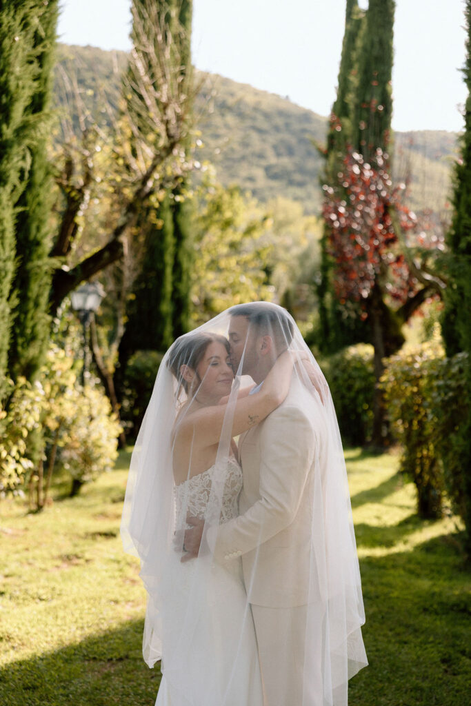 Bride and groom walking through the gardens of Villa di Piazzano in Tuscany, surrounded by cypress trees and rolling hills during an intimate destination wedding.