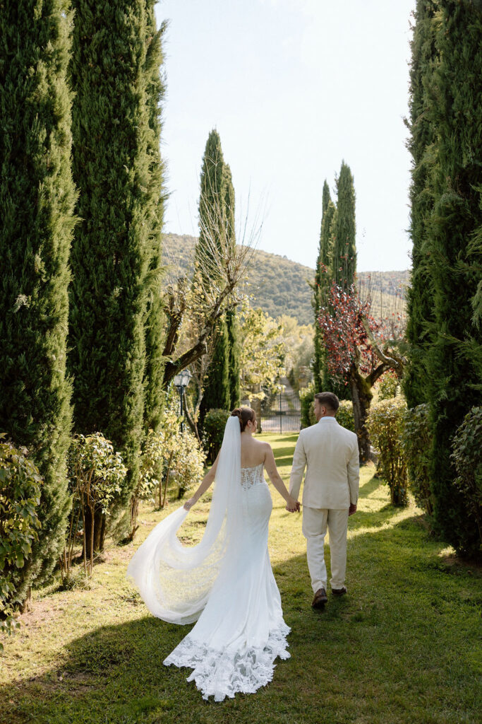 Bride and groom walking through the gardens of Villa di Piazzano in Tuscany, surrounded by cypress trees and rolling hills during an intimate destination wedding.