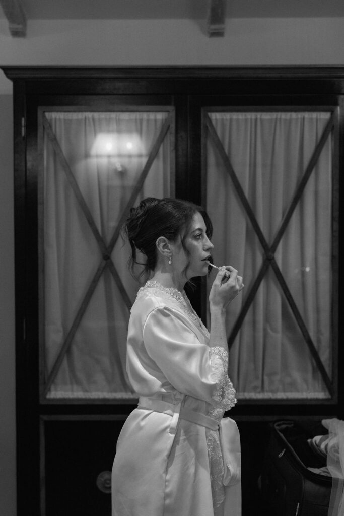 Bride wearing a lace wedding gown with corseted bodice and cathedral veil while getting ready in an antique-filled suite at Villa di Piazzano.