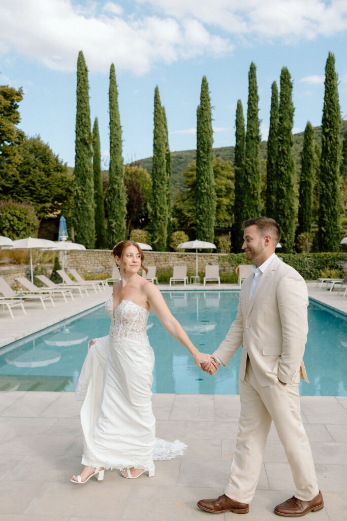 Bride and groom laughing poolside with the villa dog during portraits at Villa di Piazzano, adding a playful and personal touch to their destination wedding.