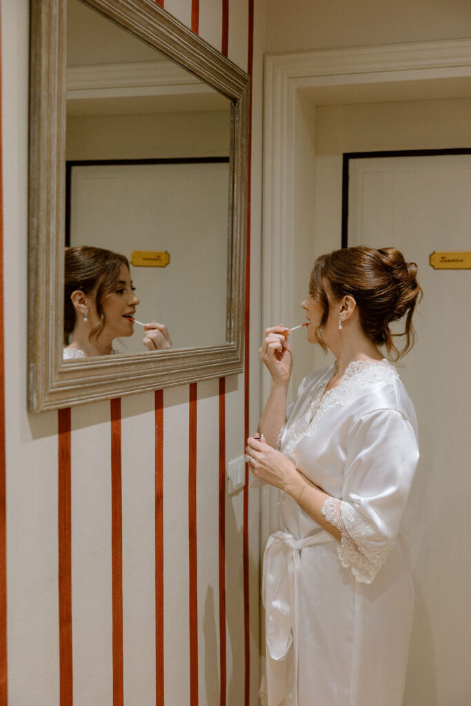 Bride wearing a lace wedding gown with corseted bodice and cathedral veil while getting ready in an antique-filled suite at Villa di Piazzano.