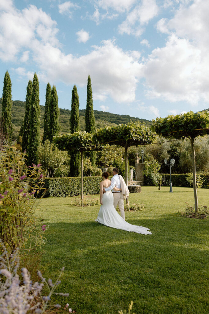Bride and groom walking through the gardens of Villa di Piazzano in Tuscany, surrounded by cypress trees and rolling hills during an intimate destination wedding.