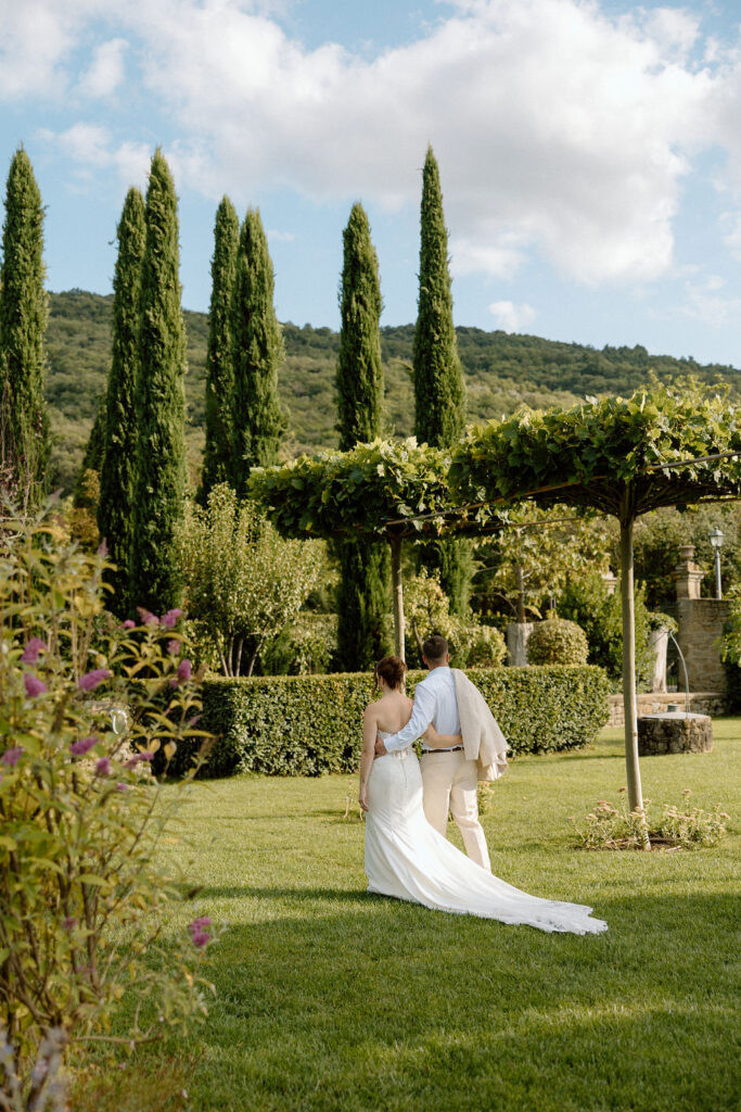 Bride and groom walking through the gardens of Villa di Piazzano in Tuscany, surrounded by cypress trees and rolling hills during an intimate destination wedding.