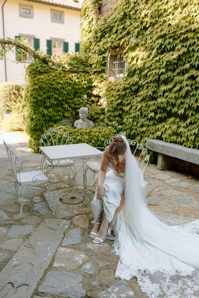 Bride wearing a lace wedding gown with corseted bodice and cathedral veil while getting ready in an antique-filled suite at Villa di Piazzano.