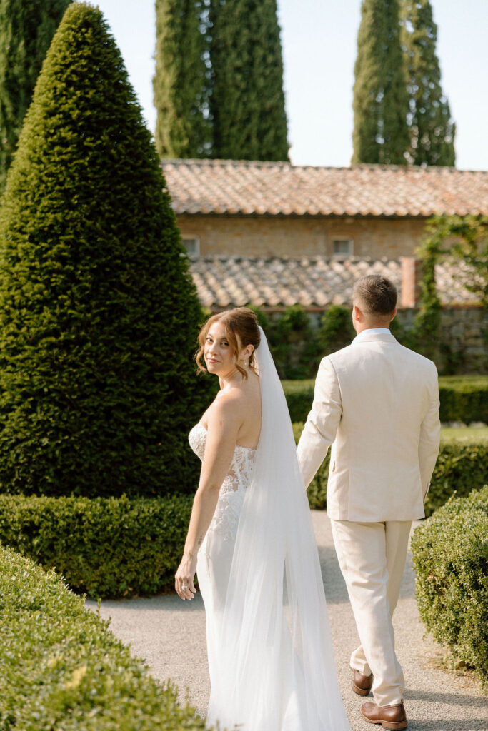 Bride and groom walking through the gardens of Villa di Piazzano in Tuscany, surrounded by cypress trees and rolling hills during an intimate destination wedding.