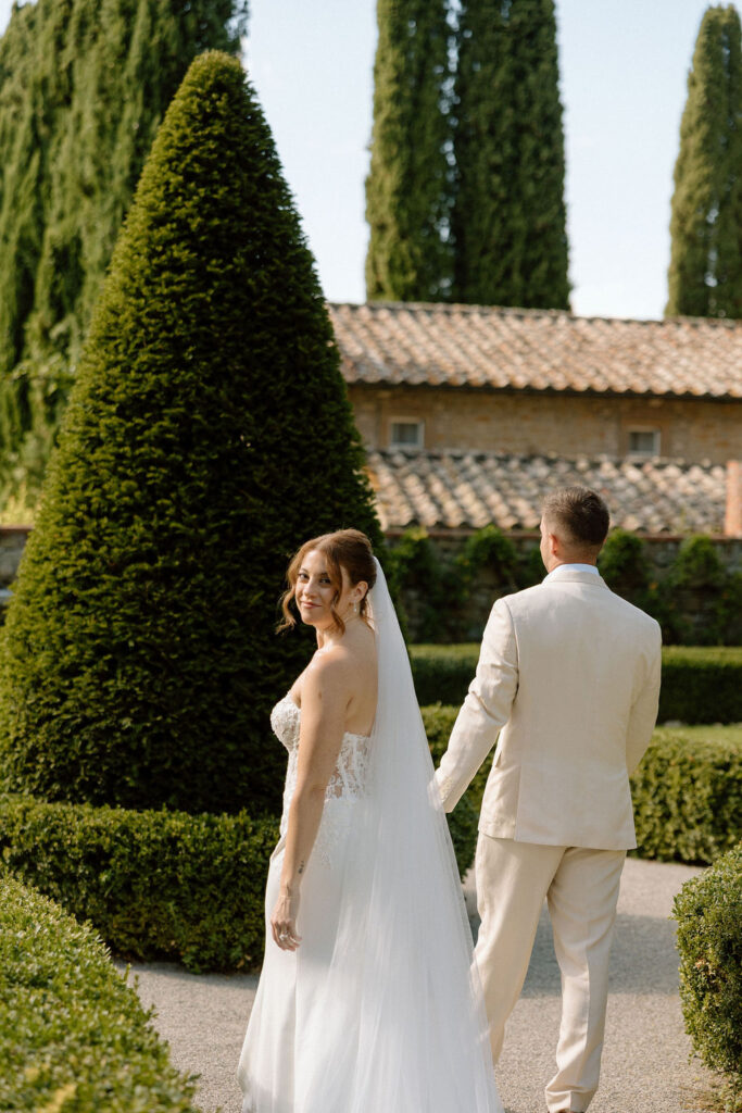 Bride and groom walking through the gardens of Villa di Piazzano in Tuscany, surrounded by cypress trees and rolling hills during an intimate destination wedding.