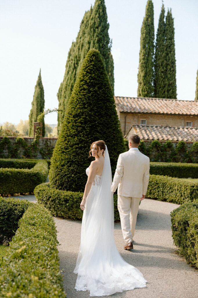 Bride and groom walking through the gardens of Villa di Piazzano in Tuscany, surrounded by cypress trees and rolling hills during an intimate destination wedding.