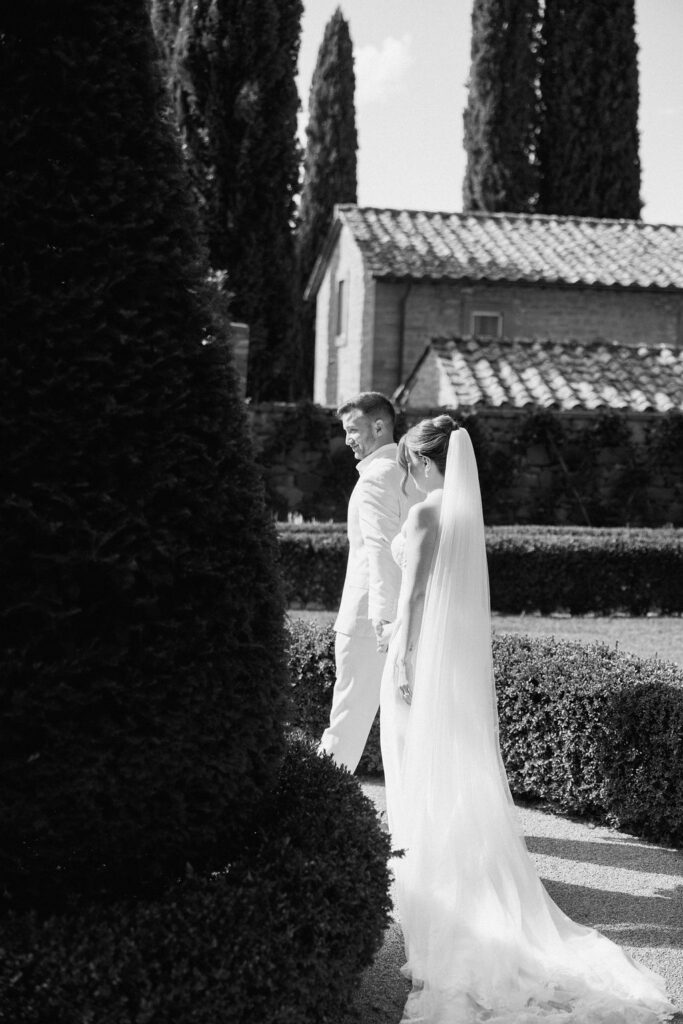 Bride and groom walking through the gardens of Villa di Piazzano in Tuscany, surrounded by cypress trees and rolling hills during an intimate destination wedding.