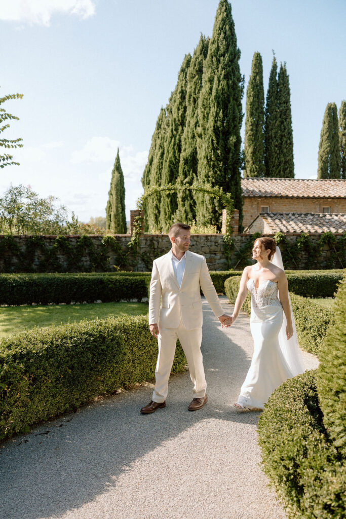 Bride and groom walking through the gardens of Villa di Piazzano in Tuscany, surrounded by cypress trees and rolling hills during an intimate destination wedding.