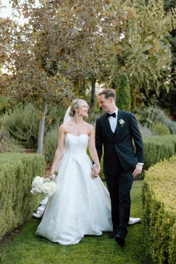 Bride and Groom walk hand in hand on their wedding day through Park Winter's garden during their luxury black tie summer wedding
