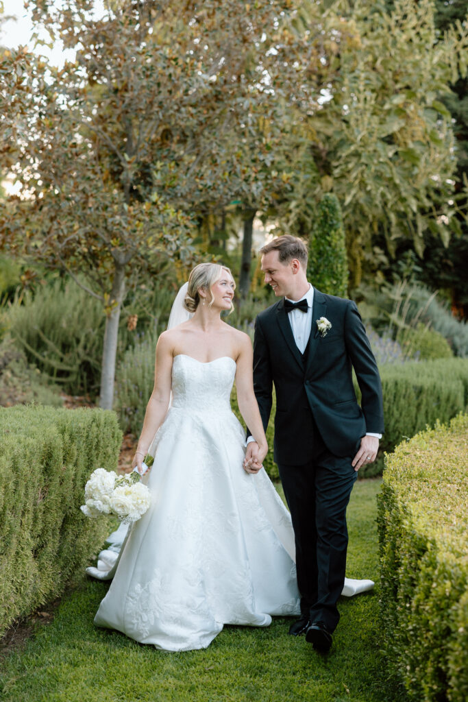 Bride and Groom walk hand in hand on their wedding day through Park Winter's garden during their luxury black tie summer wedding