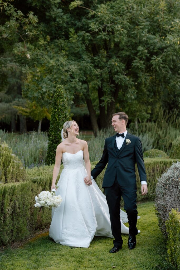 Bride and Groom walk hand in hand laughing on their wedding day through Park Winter's garden during their luxury black tie summer wedding