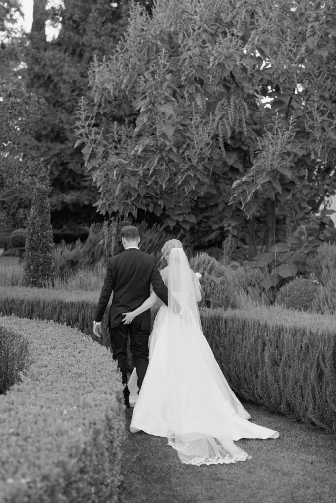 Bride and Groom walk hand in hand grabbing each other's butt on their wedding day through Park Winter's garden during their luxury black tie summer wedding