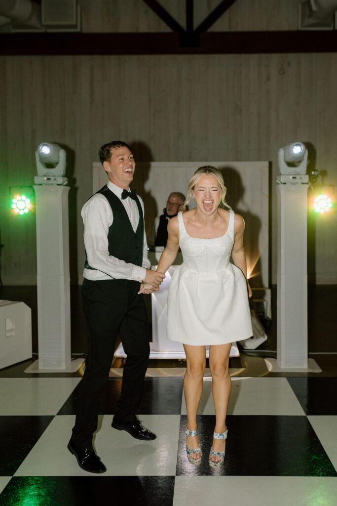 Bride and groom jump and dance excitedly with the dj in the background at their california wedding reception party