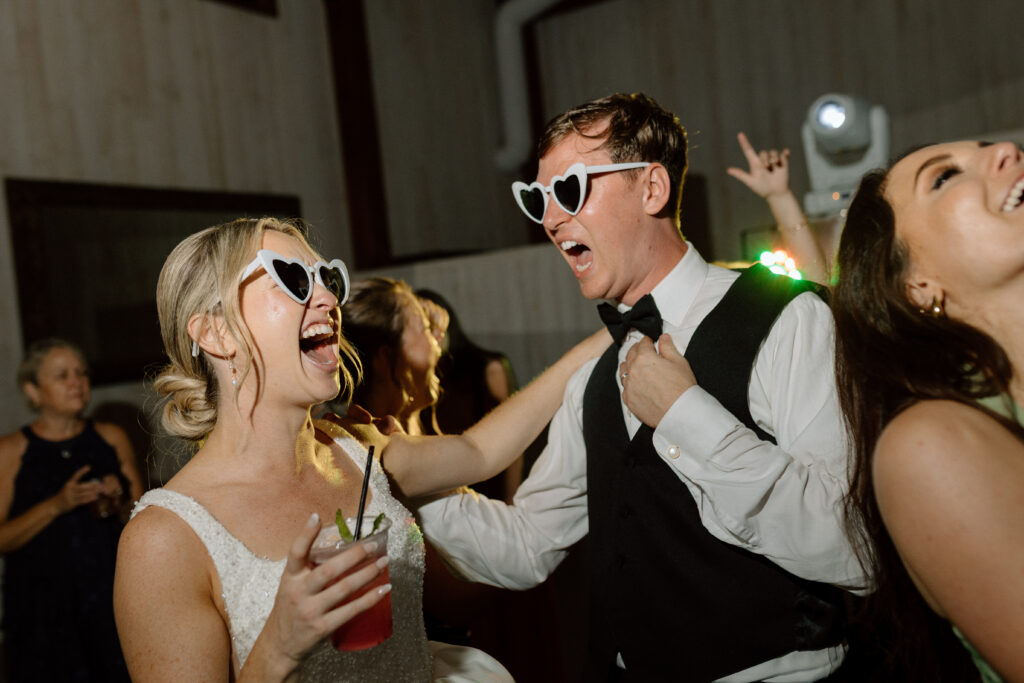 Bride and groom party happily at their reception party with heart sunglasses and drinks
