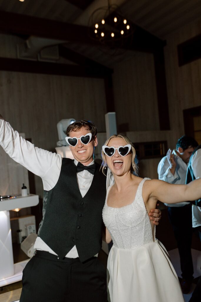 Bride and groom smile with heart sunglasses to the camera in the reception wedding clothes 
