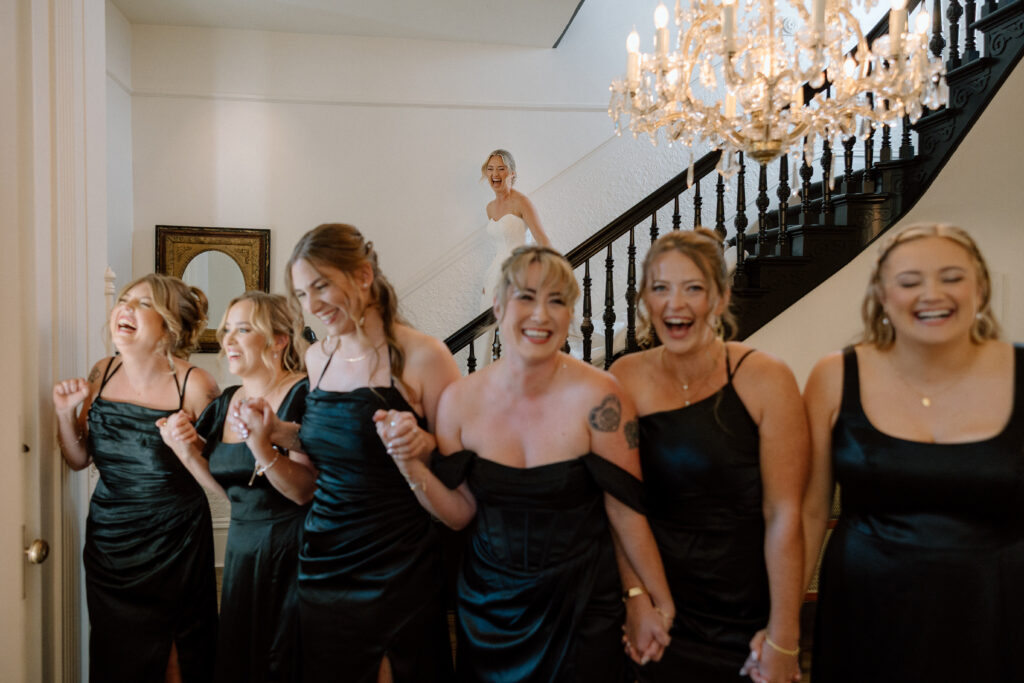Bride comes down Park Winters staircase to show off her wedding dress to her waiting bridesmaids 