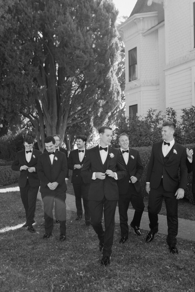 Editorial photo of groom walks with groomsmen all in black suits on wedding day 