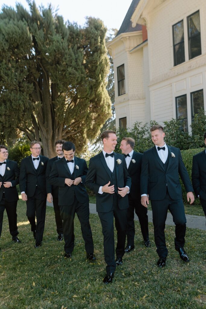 Editorial photo of groom walks with groomsmen all in black suits on wedding day 