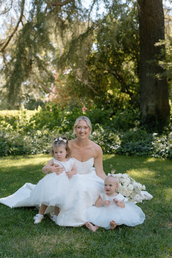 Brides poses with flower girls in little white dress in the garden at Park Winters