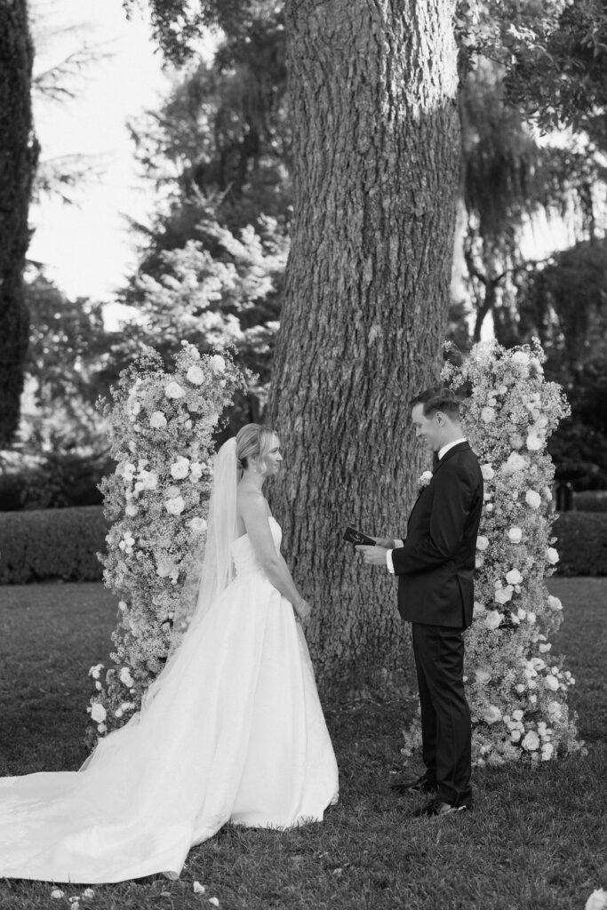 bride and groom share vows with floral arch behind them captured by california wedding photographer