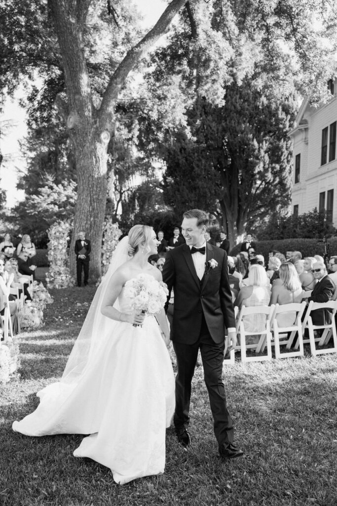 walking down the aisle with floral arch behind them and guests clapping captured by california wedding photographer