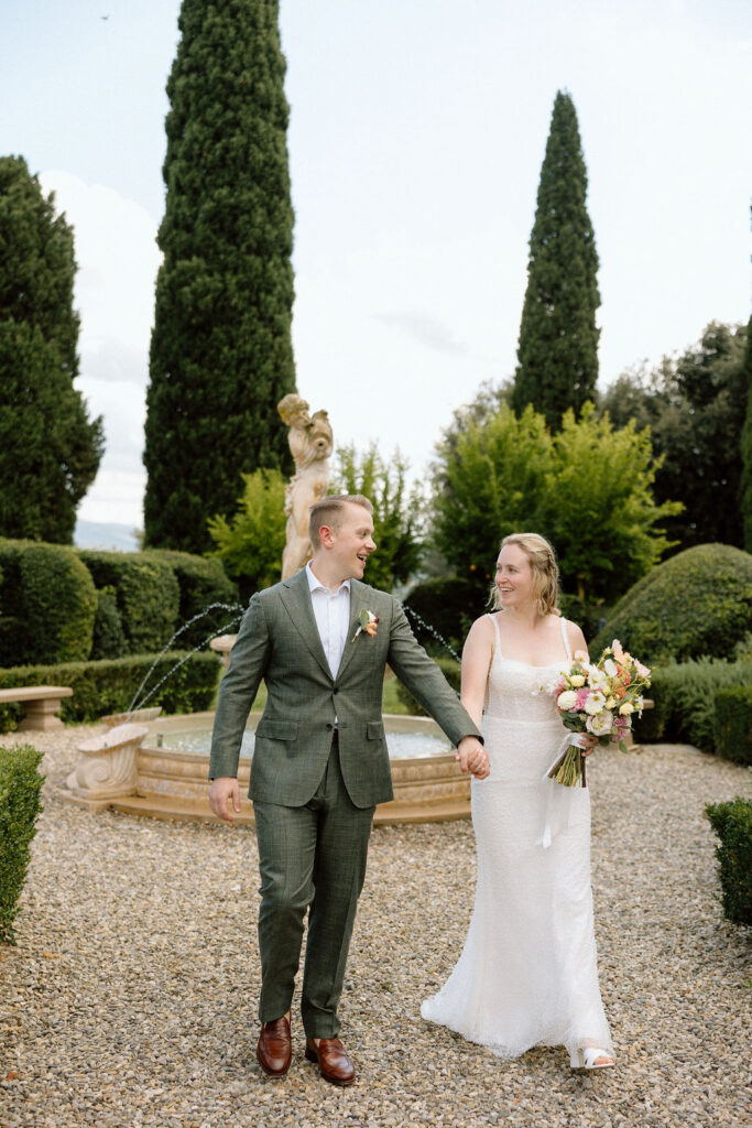 Bride and groom walking through garden paths of the historic villa after their elopement with stone architecture and olive trees.